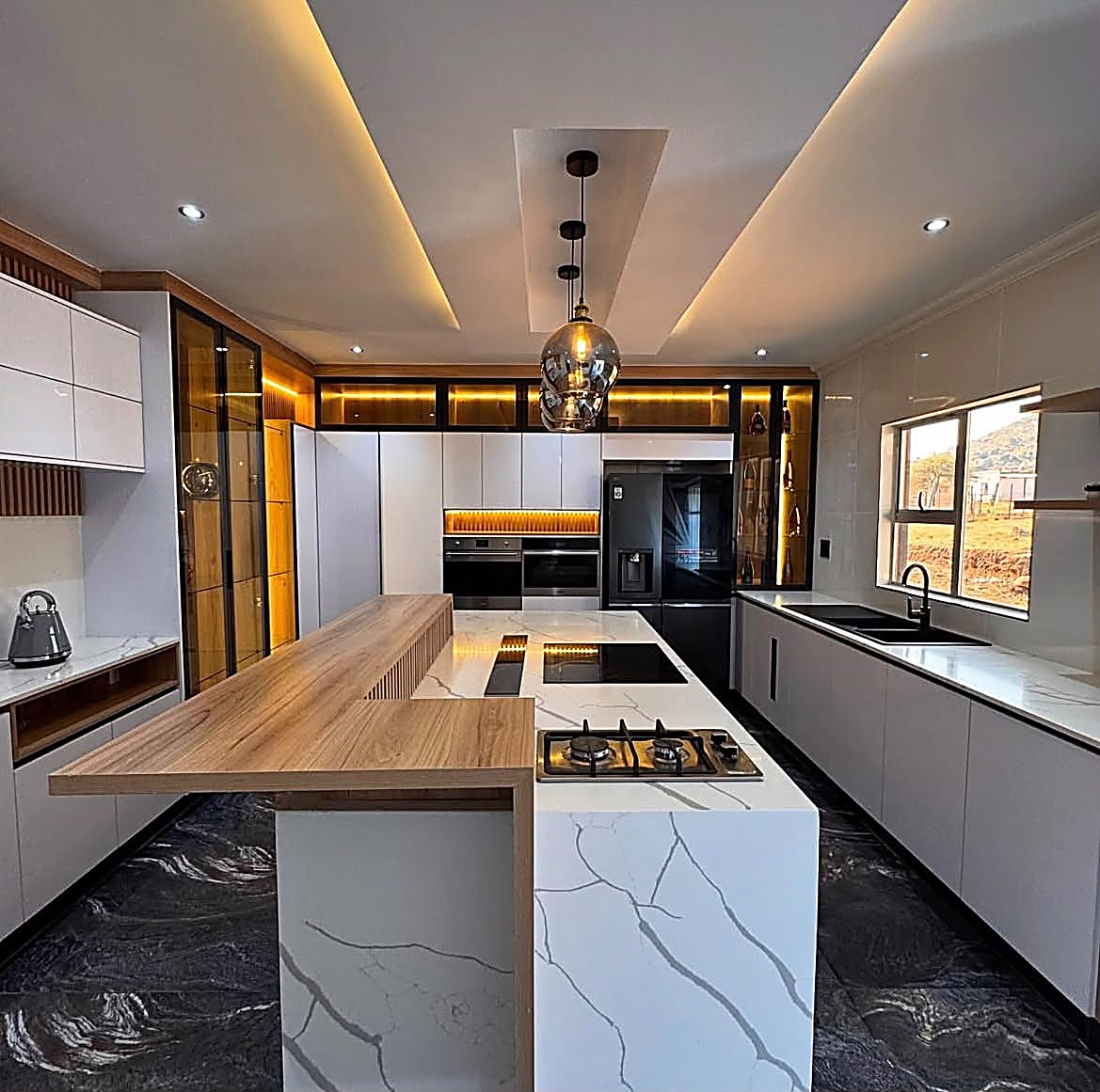 Kitchen Units — White handleless kitchen with marble-look island, wood breakfast bar, LED-lit display cabinets and pendant lighting — custom cabinetry by Epique Interiors.